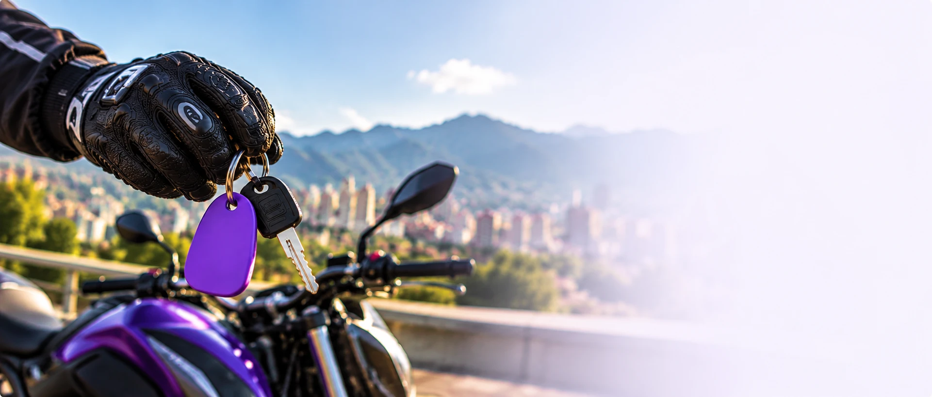 Mano con guante sosteniendo las llaves con llavero morado frente a una moto